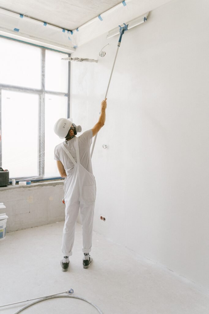 Adult painter in white uniform painting an indoor wall with a roller.