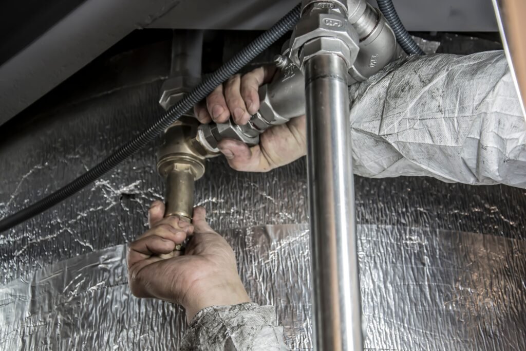 أفضل شركة صيانة سباكة فلل في أبوظبي 0547761290 Close-up of a plumber's hands installing steel pipes indoors, showcasing skilled manual work.